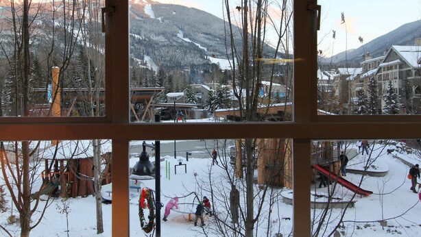 A view through a window of a ski resort with snow-covered slopes, buildings, and a clear sky.