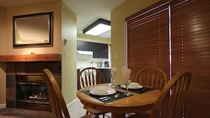 A dining area with a wooden table set for four, a fireplace, and a kitchen in the background. - Marketplace Lodge #245 | Studio with Kitchen, Fireplace, and Balcony (Whistler)