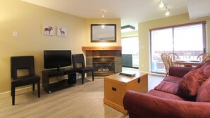 A living room with a fireplace, a television, and a red sofa. - Marketplace Lodge #245 | Studio with Kitchen, Fireplace, and Balcony (Whistler)