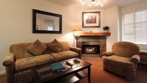 Una sala de estar con sofá, sillón, chimenea y una mesa de centro con libros y un control remoto.