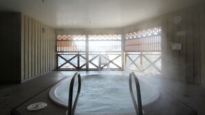 A hot tub in a room with a view of a building through a window with a lattice design.