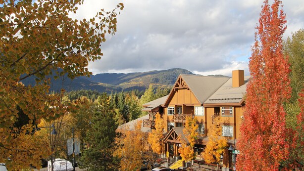 A lodge with a mountain backdrop, a parking area, and autumn foliage.