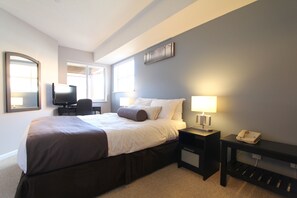 A hotel room with a bed, bedside tables, a desk with a chair, a television, and a window.
