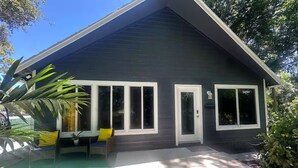 Una casa moderna con fachada oscura, amplias ventanas y un porche cubierto con mobiliario exterior.