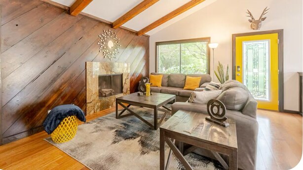Una sala de estar acogedora con techo de madera, un sofá con cojines amarillos, una mesita de centro y una chimenea.