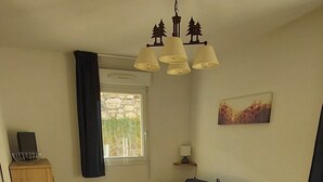 Een zithoek met een tafel en stoelen, een bank, een raam met gordijnen, een radiator en een plafondlamp.