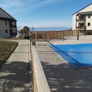 A swimming pool with a wooden deck, a view of mountains, and a fenced area. - A Thousand Suns (Font-Romeu-Odeillo-Via)