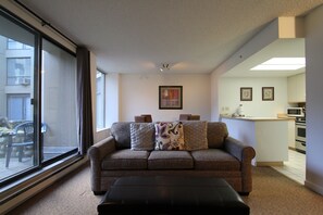 A living room with a sofa, ottoman, and a view through a large window.