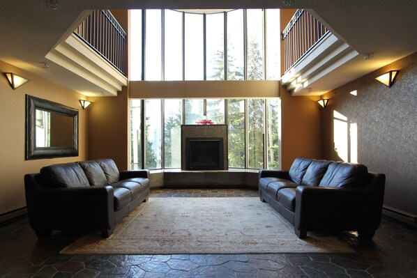 A spacious living room with a fireplace, two leather sofas, a large rug, and a stone floor.