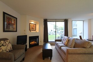 A living room with a fireplace, a television, a sofa, and a large window.