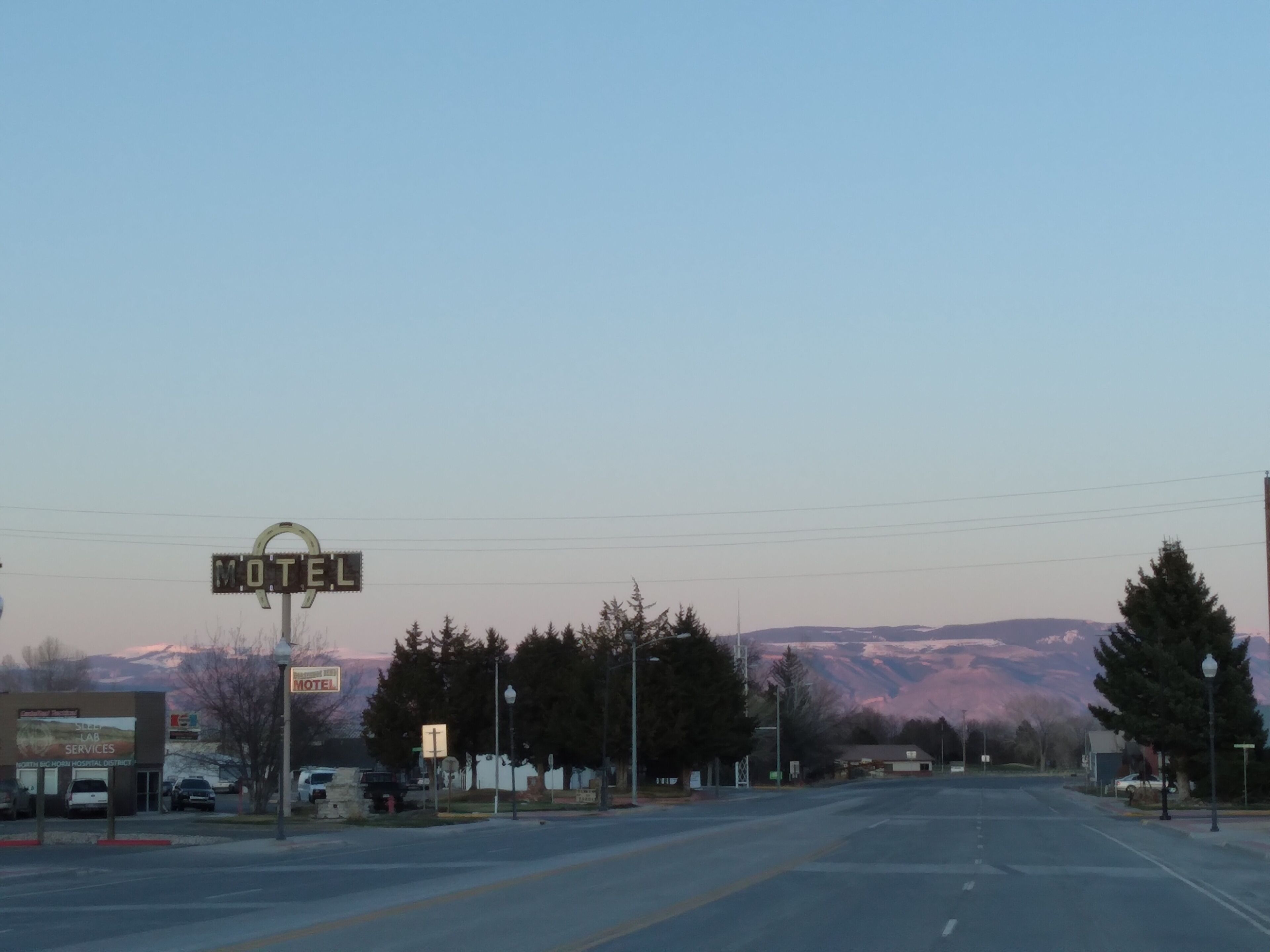 A motel with a large sign, a road in the foreground, and mountains in the background.