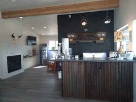 A spacious room with a wooden ceiling, a fireplace, a bar area with a laptop, and a vintage-style sign.