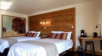 A room with two beds, a wooden headboard, a desk with a lamp, and a painting of a buffalo.