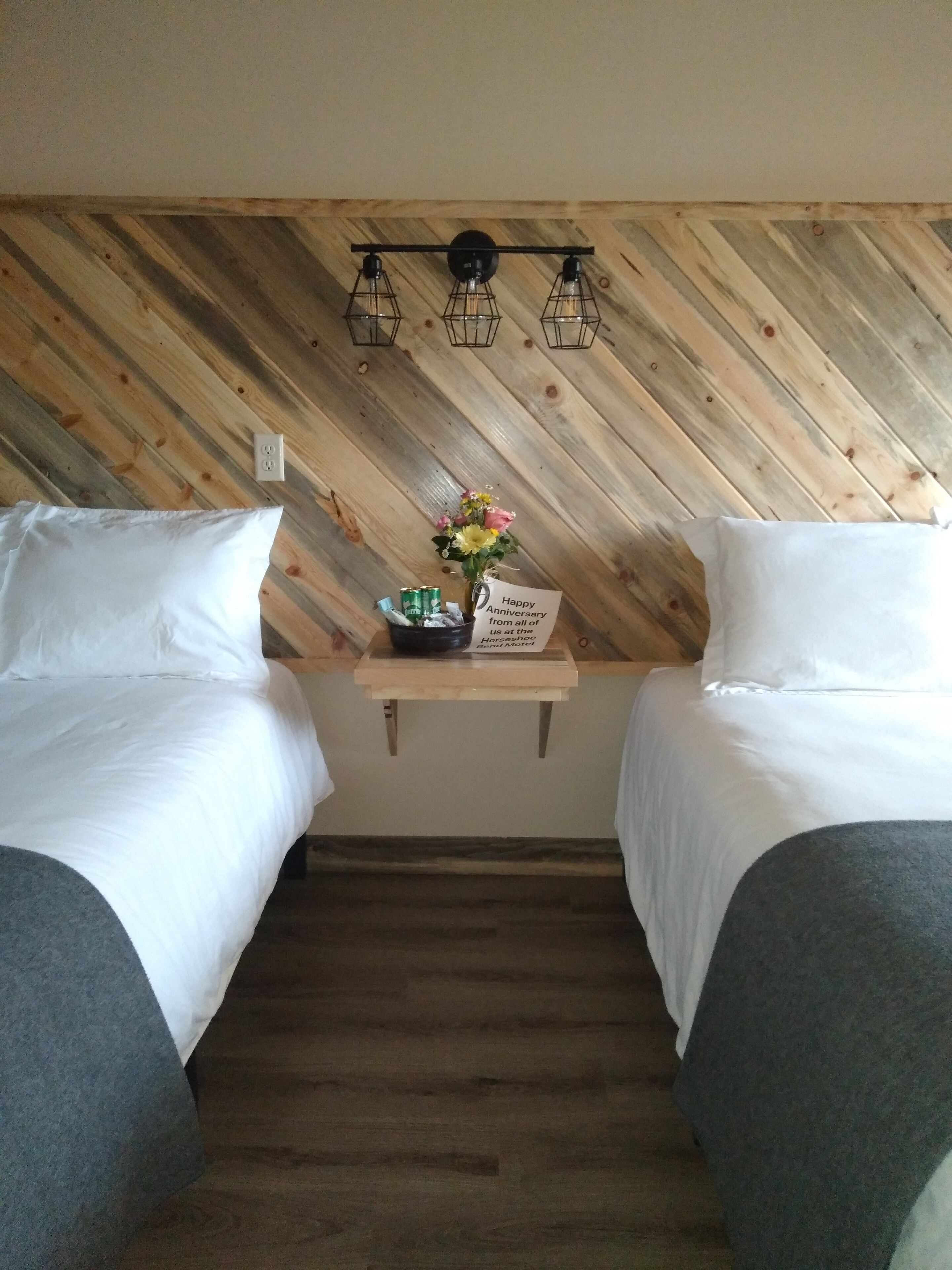 A hotel room with two beds, a wooden slat ceiling, a small table with a flower arrangement and a card, and a wooden floor.