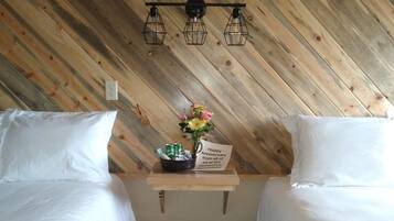 A hotel room with two beds, a wooden slat ceiling, a small table with a flower arrangement and a card, and a wooden floor.