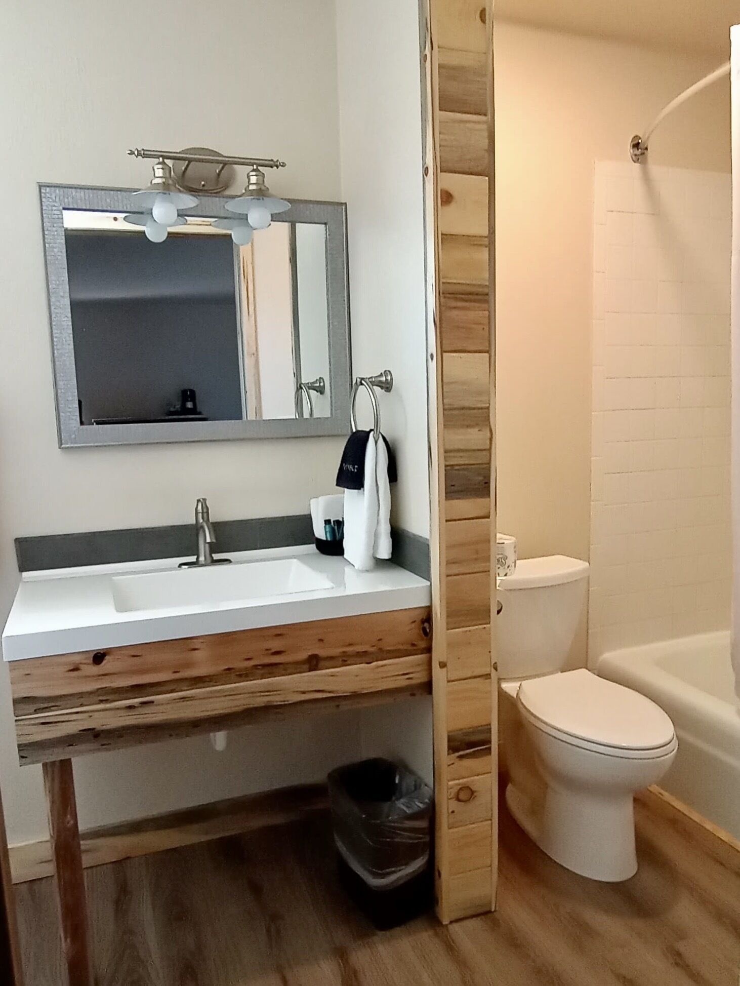 Un baño con tocador de madera, lavamanos, espejo, toalla, inodoro y ducha.