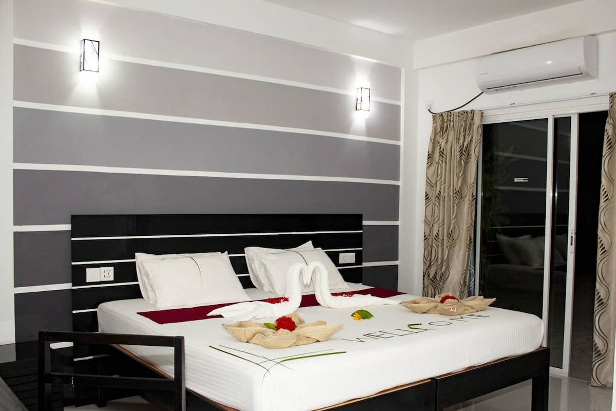 Una habitación de hotel moderna con una cama grande, una mesita de noche, aire acondicionado empotrado y una puerta de vidrio corredera con cortinas.
