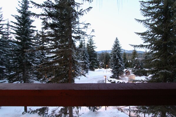A snowy landscape with evergreen trees and a distant building, viewed from a wooden railing.