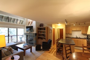 Een ruime woonkamer met een open haard, een eettafel en een keuken met houten kastjes.