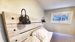 Un dormitorio con cabecera de madera, una ventana con vistas a árboles y una mesita de noche con una lámpara.