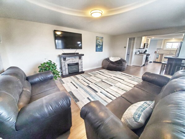 A living room with a fireplace, leather sofas, a flat-screen TV, and a kitchen in the background.