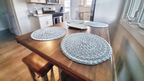 Una cocina con armarios de madera, un microondas y una mesa de comedor con individuales tejidos.