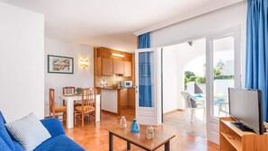 A compact living space with a dining area, kitchenette, and a balcony with a TV. - Arena 2 bedroom villa, Cala Blanca (Ciutadella de Menorca)