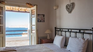 A bedroom with a bed, a nightstand, a lamp, a heart-shaped decoration, and a view of the sea.