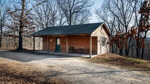 Une cabane rustique dotée d’un porche abrité, d’une table et de chaises, et d’une porte verte.