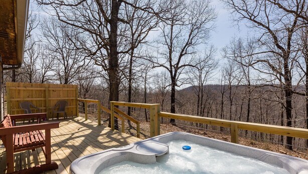 Un bain à remous sur une terrasse en bois, avec vue sur des arbres sans feuilles et des collines en arrière-plan.