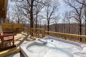 Un bain à remous sur une terrasse en bois, avec vue sur des arbres sans feuilles et des collines en arrière-plan.