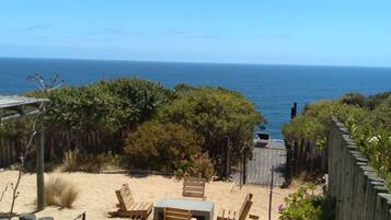 A beach with wooden chairs and a table, a wooden fence, and a view of the ocean.