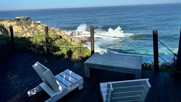 Une terrasse en bois avec des chaises longues blanches donnant sur l’océan.