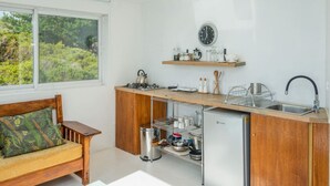 Une cuisine compacte avec un banc en bois, un petit réfrigérateur et une fenêtre donnant sur un espace verdoyant.