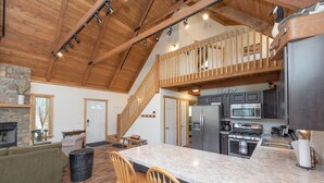 A spacious kitchen with a large island, wooden ceiling beams, and a stone fireplace. - Cozy Mountain Retreat w/ Hot Tub & Fire Pit (Swanton)