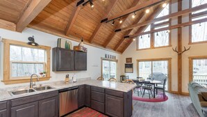 A spacious kitchen with dark wooden cabinets, a granite countertop, and a red rug. - Cozy Mountain Retreat w/ Hot Tub & Fire Pit (Swanton)