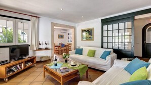 A living room with a television, sofa, coffee table, and a dining area in the background. - Ca'n Toni 3 bedroom villa, Cala Galdana (Cala Galdana)