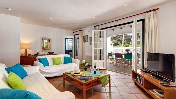 A living room with a sofa, coffee table, TV, and a view of the outside patio. - Ca'n Toni 3 bedroom villa, Cala Galdana (Cala Galdana)