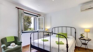 A bedroom with a single bed, a green armchair, a small bedside table with a lamp, and a window with curtains. - Ca'n Toni 3 bedroom villa, Cala Galdana (Cala Galdana)