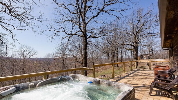 Een hottub op een houten terras met uitzicht op bomen en een afgelegen chalet.
