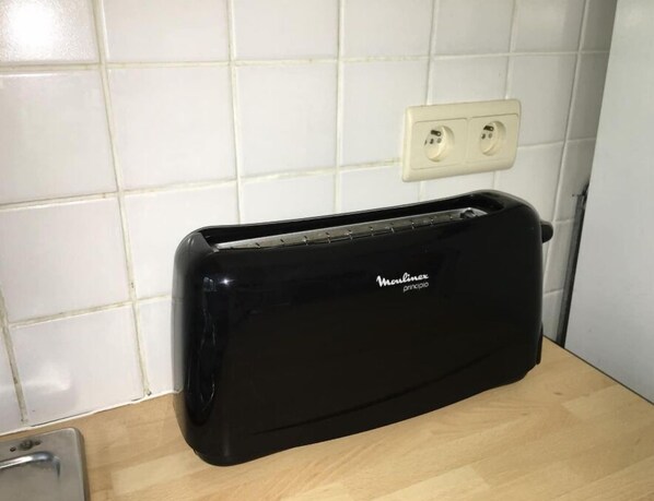 Ein schwarzes Toaster auf einer Holzauszugplatte mit weiß gefliestem Fliesenspiegel und einer Steckdose darüber.