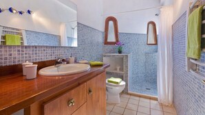 A bathroom with a wooden vanity, a sink, a mirror, and a shower area.