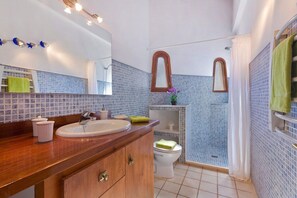 Un baño con tocador de madera, lavamanos, espejo y zona de ducha.