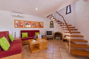 A living room with a red sofa, a wooden coffee table, a TV, and a fireplace. There is a staircase with wooden steps and a white railing. - Gerard 4 bedroom villa, Cala Blanca (Cala Blanca)