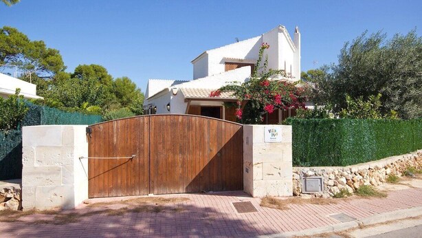 A villa with a wooden gate, a stone wall, and a clear blue sky.