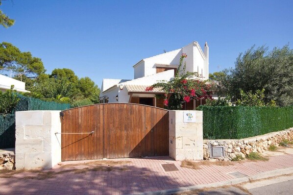 Una villa con un portón de madera, un muro de piedra y un cielo azul despejado.