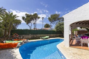 Una piscina con sillones de descanso, una pérgola y vistas a árboles y edificios al fondo.