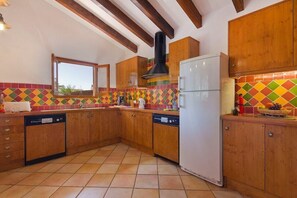 A kitchen with wooden cabinets, a white refrigerator, and colorful tile backsplash. - Gerard 4 bedroom villa, Cala Blanca (Cala Blanca)