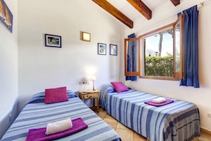 Ein Zimmer mit zwei Betten, jeweils mit gestreifter Bettdecke und Kissen, einem Nachttisch mit Lampe und einem Fenster mit Vorhängen.
