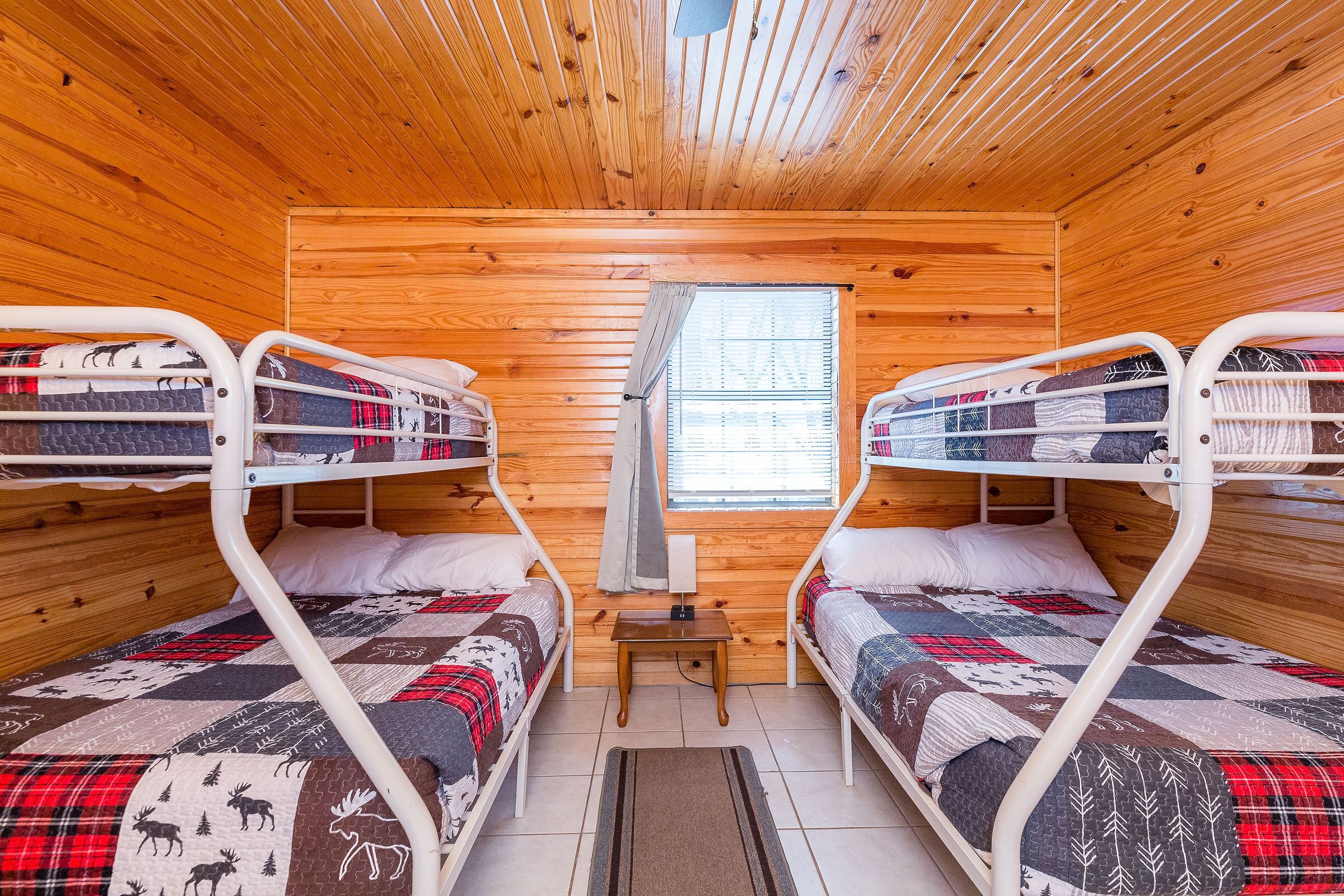A cabin with two bunk beds, wooden walls, a small table, and a window.